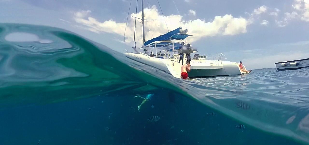 Half-underwater view of a catamaran anchored in clear water with swimmers